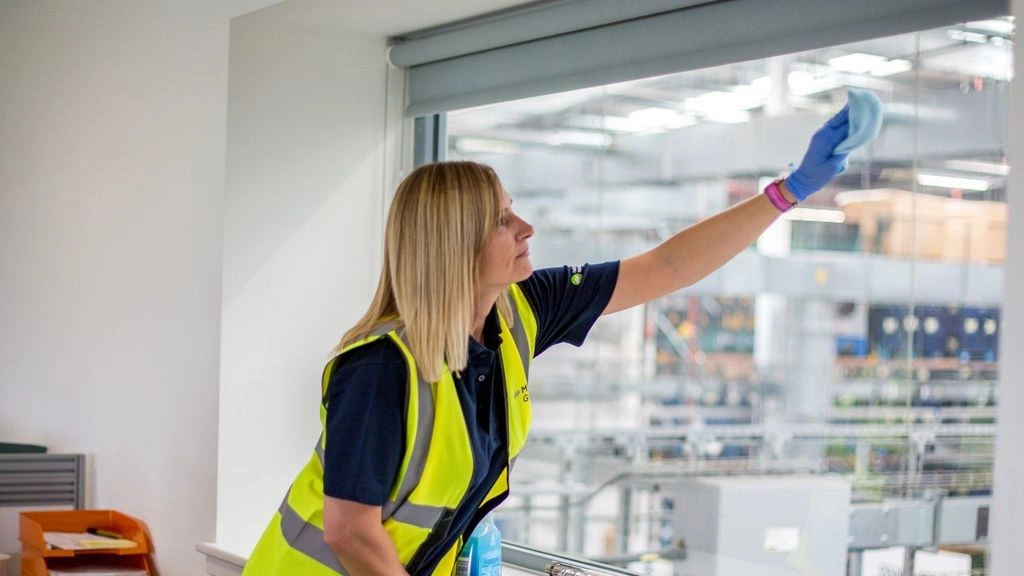 A woman in a hi-vis jacket cleaning an office window with a cloth